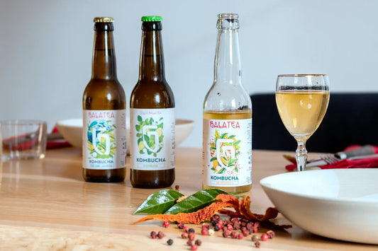 Écorces d'orange amère, feuilles de bigaradier, poivre du Sichuan et baies roses autour d'une bouteille de kombucha Hespérides