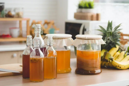 Femme tenant une bouteille de kombucha artisanal dans une cuisine moderne avec ingrédients naturels frais