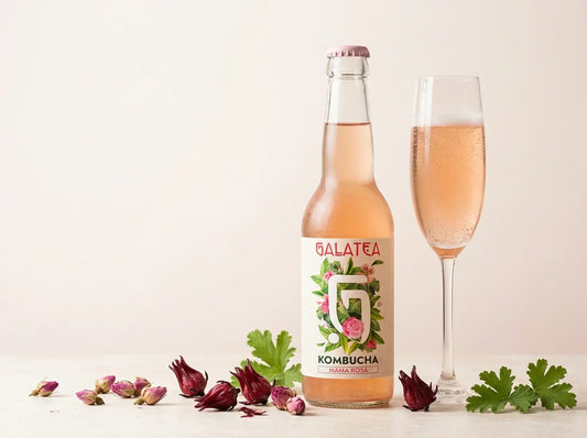 Bouteille de kombucha Mama Rosa à l'hibiscus et à la rose et flûte rose pâle, entourées de boutons de rose et de calices d'hibiscus séchés